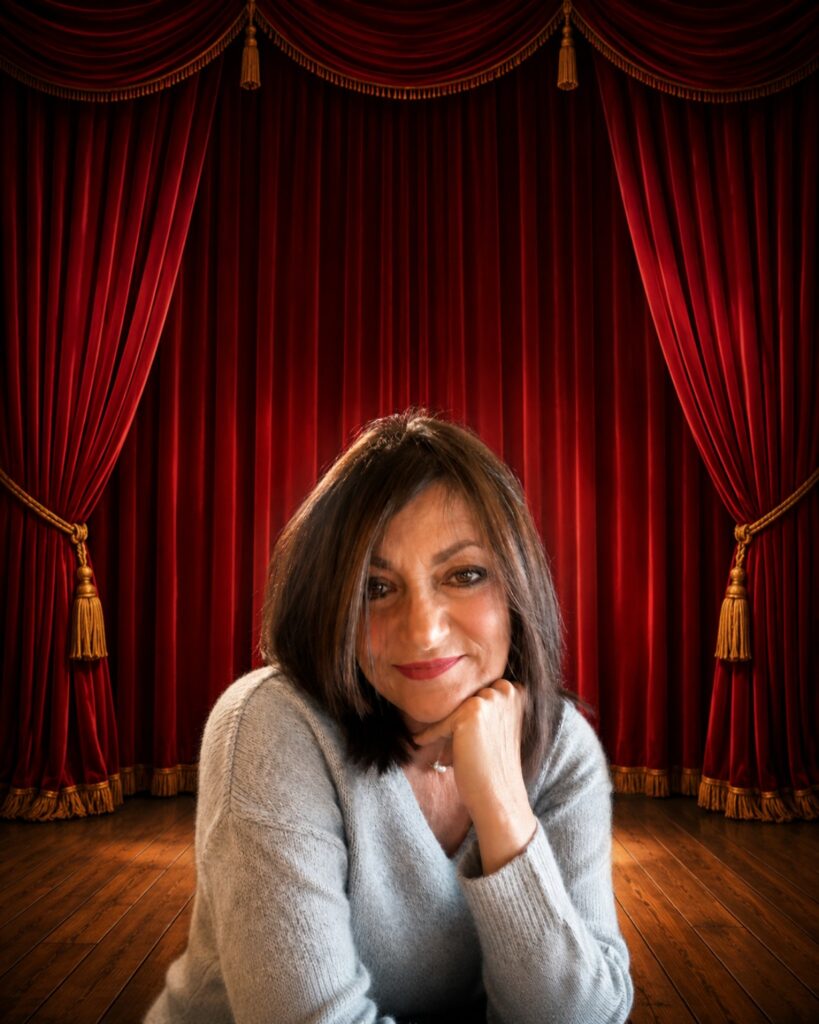 Ornella Semino autrice  di copioni teatrali e commedie, davanti a un sipario teatrale rosso